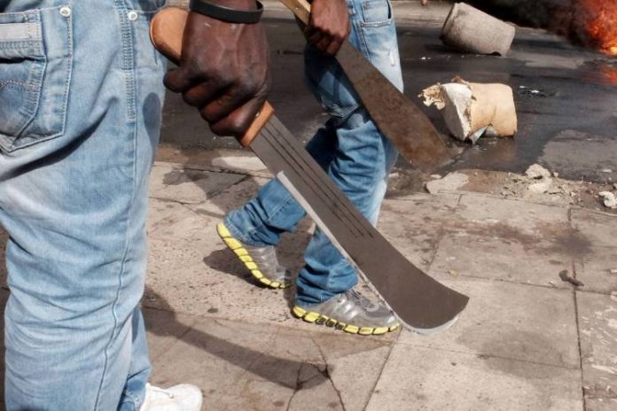 Immigrant men armed with machetes make their way onto a Durban, South Africa, street during clashes with police and in search of locals that attacked foreign shop owners in the city center, April 14, 2015 . (AP Photo/Tebogo Letsie)