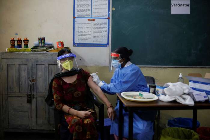 A healthcare worker gives a dose of COVISHIELD, a coronavirus disease (COVID-19) vaccine manufactured by Serum Institute of India, to a woman inside a classroom of a school, which has been converted into a temporary vaccination centre, in India
