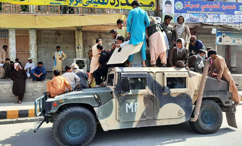 Taliban fighters and local residents sit over an Afghan National Army (ANA) humvee vehicle along the roadside in Laghman province on August 15, 2021. (Photo by - / AFP)
